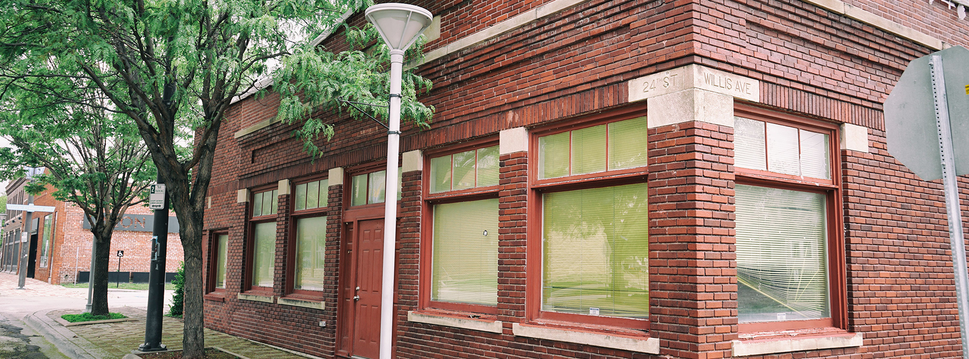 Banner photo of the FJ Carey Block building on the corner of North 24th and Willis Avenue The red brick building has a red door and two locust trees growing in front