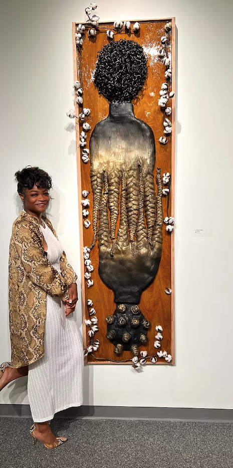 Exhibiting Artist Lily Stennis Vinson standing and smiling next to one of her artworks