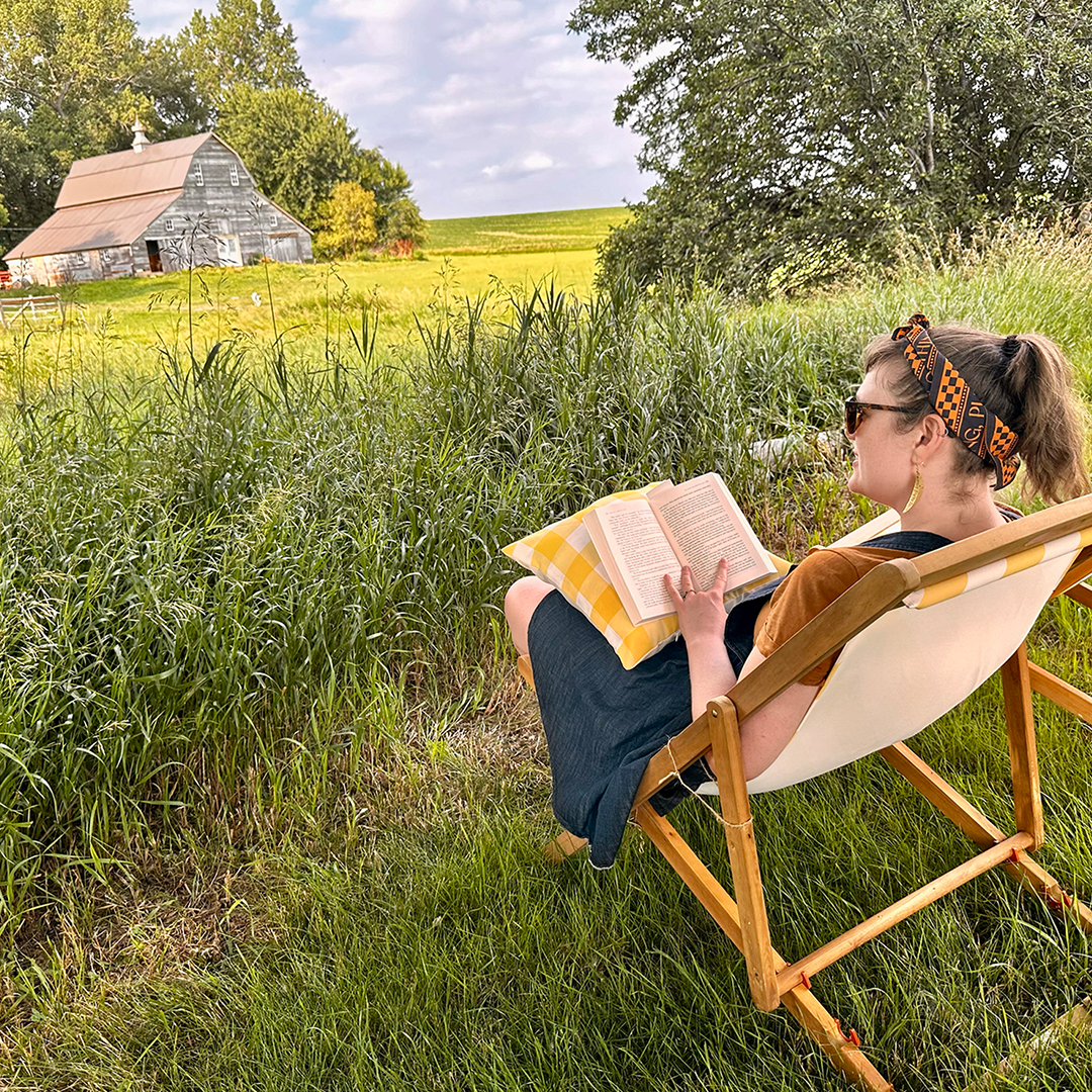 Populus Fund Grantee Chicken Coop Residency Square A person sits in a lush green field with an old barn in the background